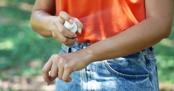 Person spraying bug spray on their arm
